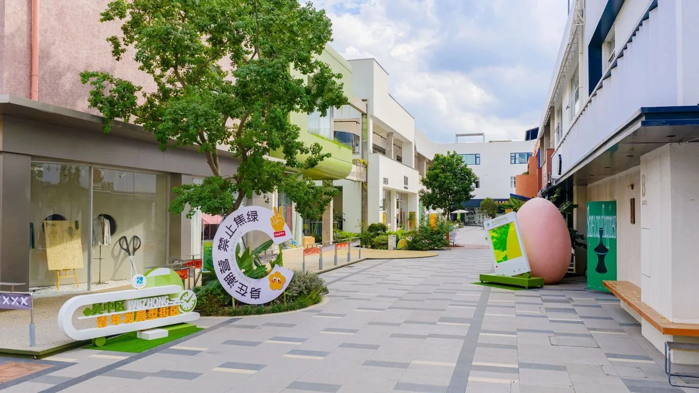 时差市界街区内部，彩色店招与绿植沿街展开