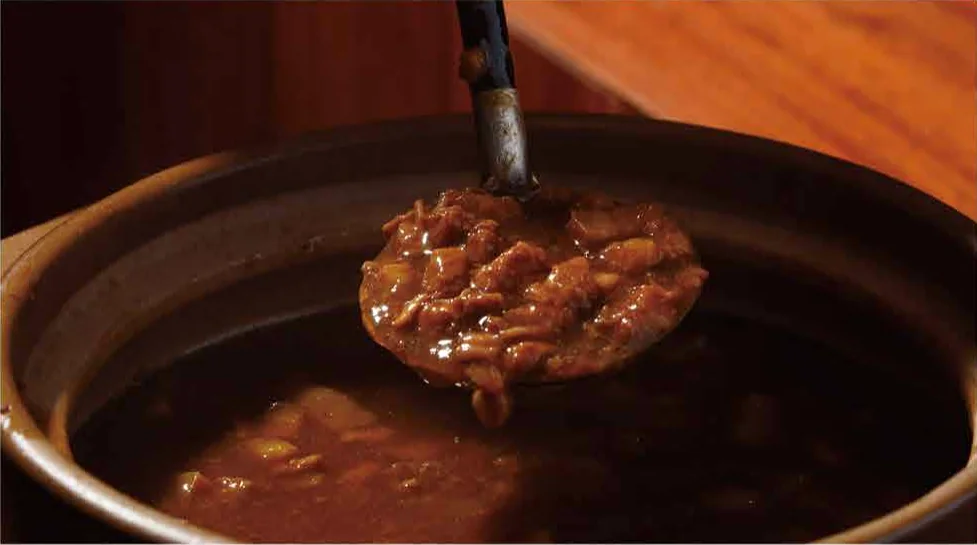 Braising gravy and a long-handled ladle in a clay pot